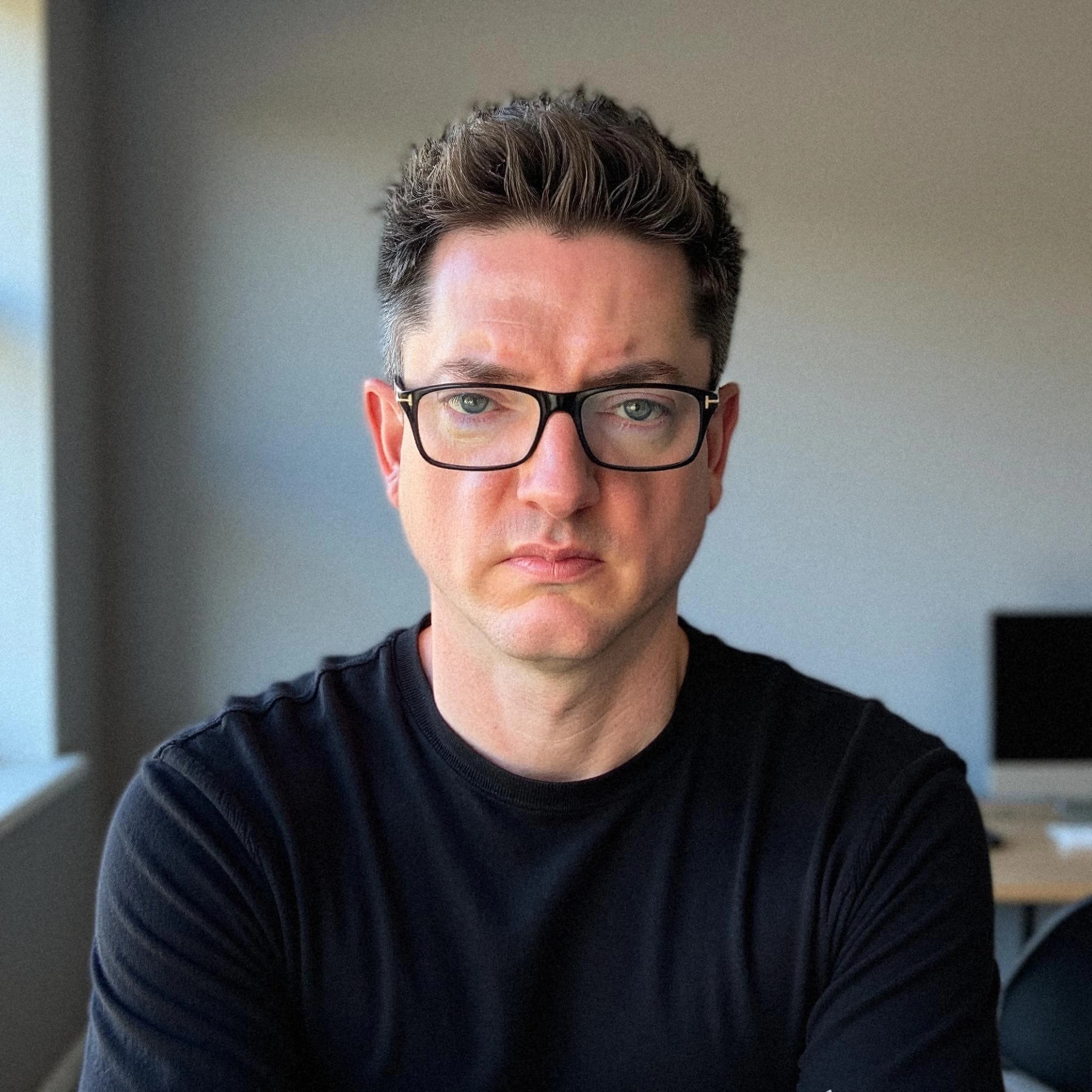 Professional headshot example: Man Office Black Shirt Sitting — LinkedInHeadshots.ai