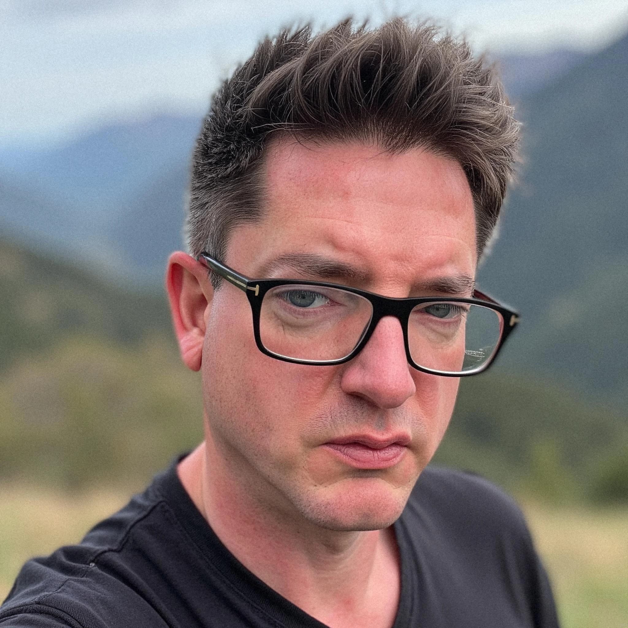 Professional headshot example: Man Outdoors Black Shirt Glasses — LinkedInHeadshots.ai