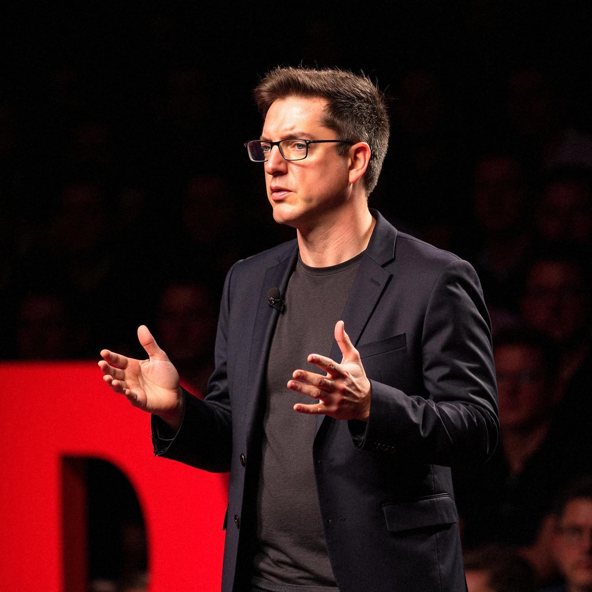 Professional headshot example: Man Stage Black Suit Talking — LinkedInHeadshots.ai