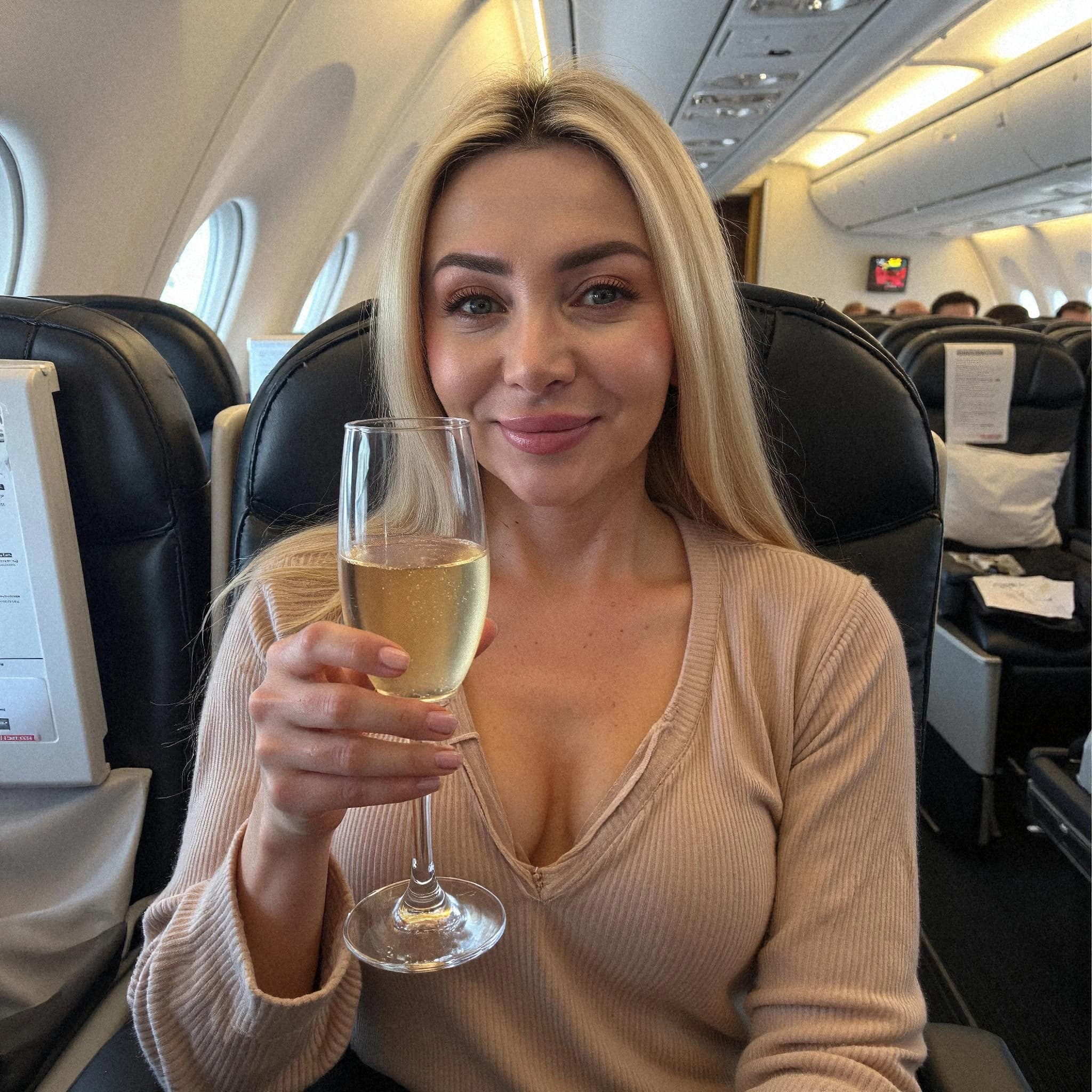 Professional headshot example: Woman Airplane Beige Top Holding Champagne — LinkedInHeadshots.ai