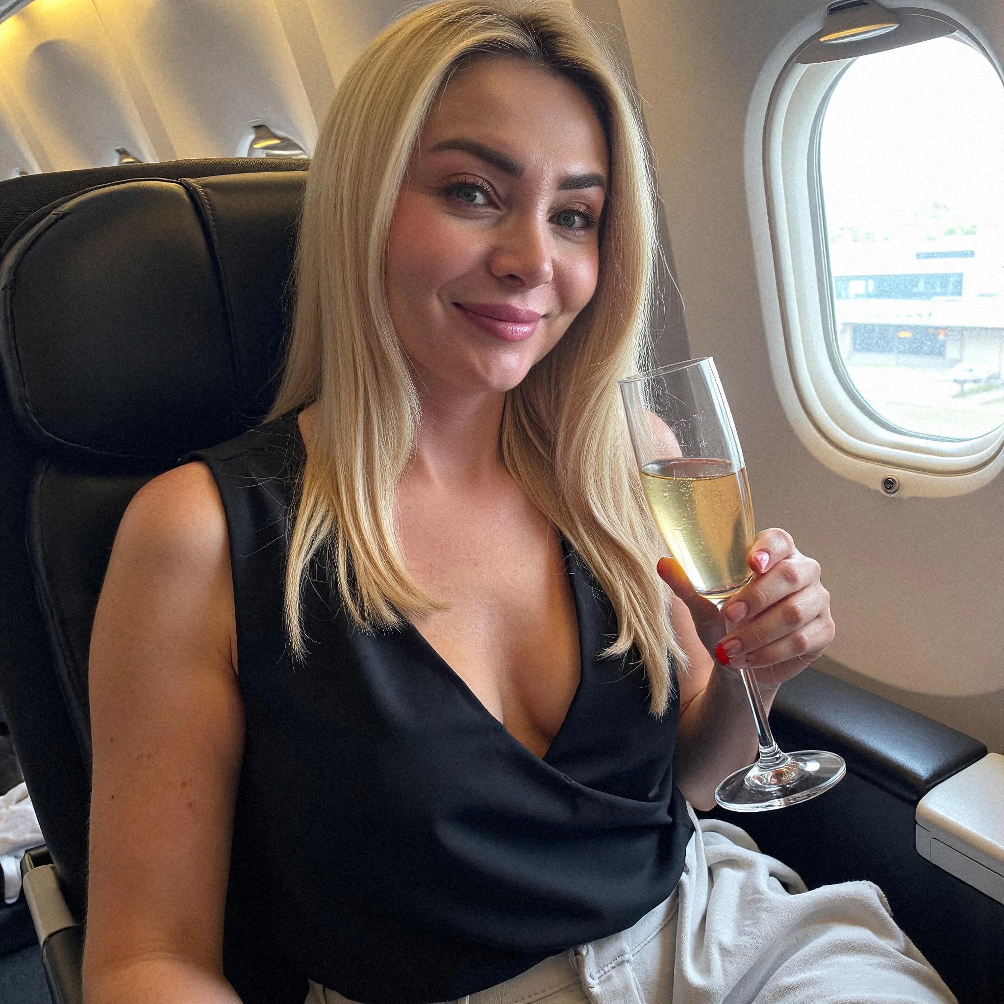 Professional headshot example: Woman Airplane Black Top Holding Champagne — LinkedInHeadshots.ai