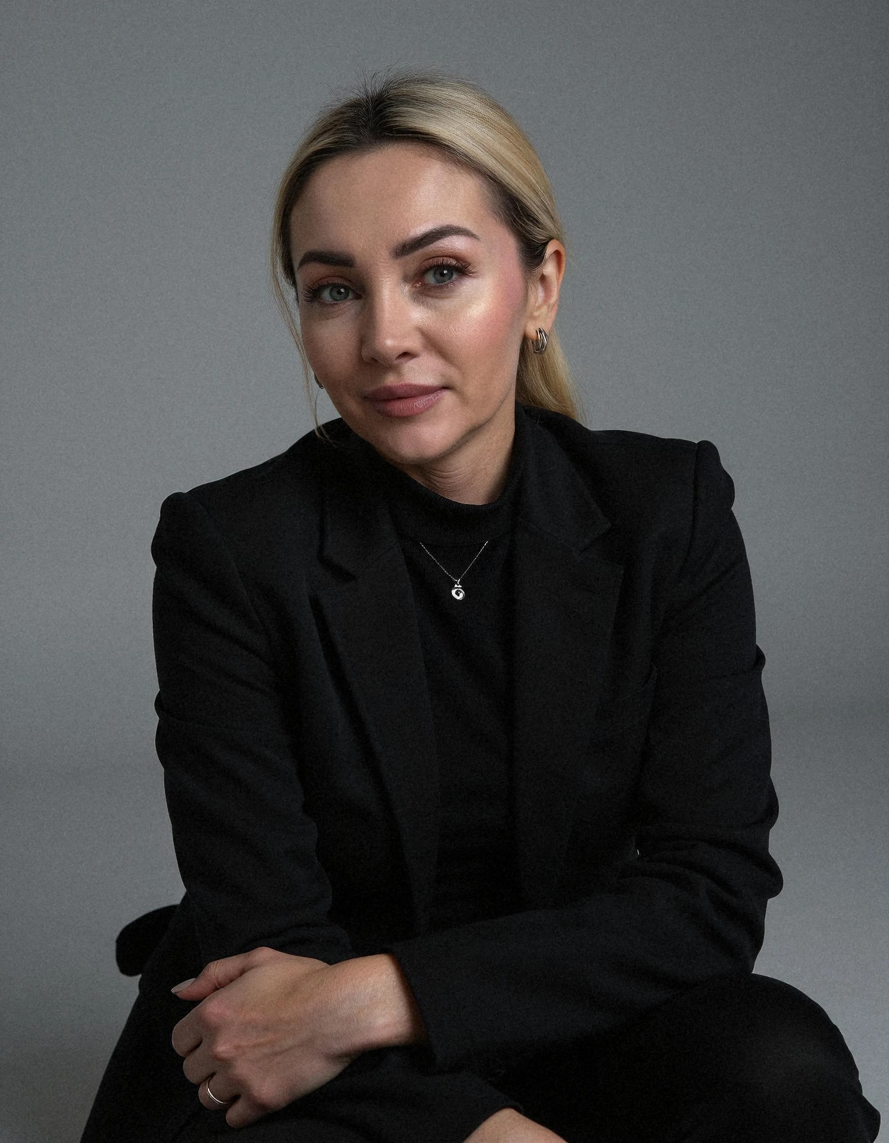 Professional headshot example: Woman Studio Black Suit Sitting — LinkedInHeadshots.ai