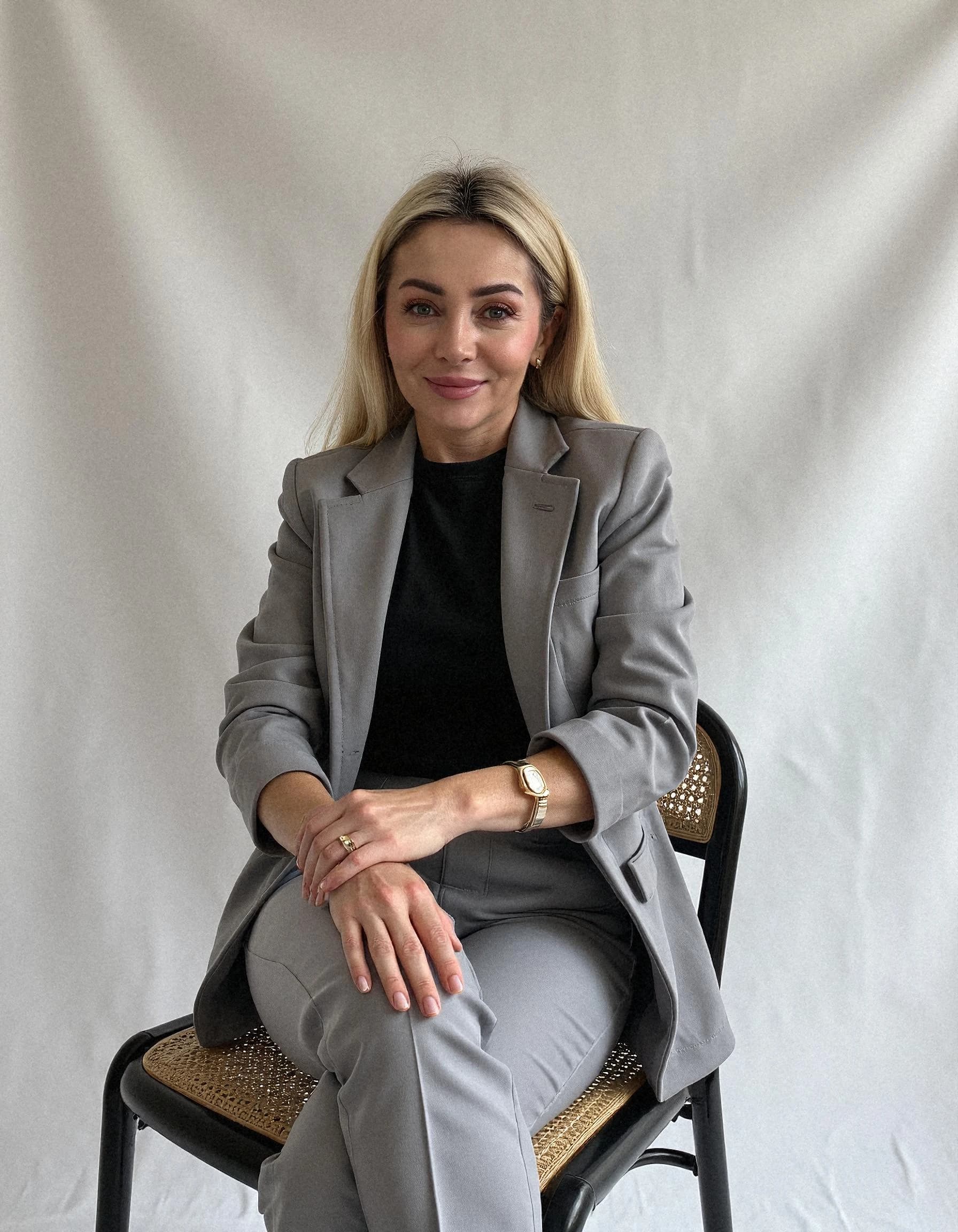 Professional headshot example: Woman Studio Gray Suit Sitting — LinkedInHeadshots.ai